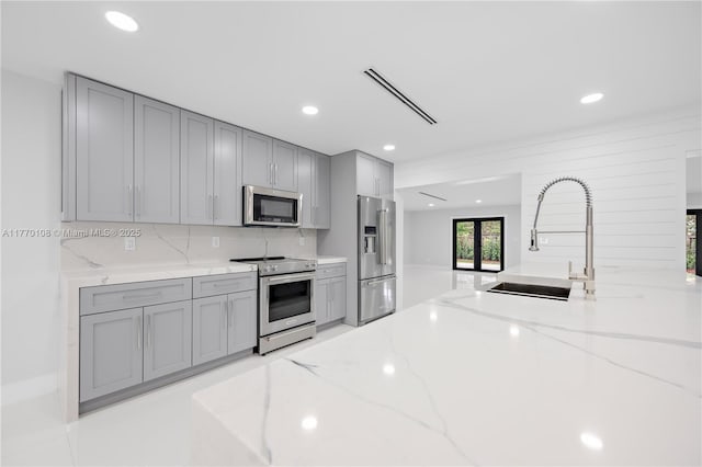 kitchen featuring gray cabinets, stainless steel appliances, backsplash, a sink, and visible vents