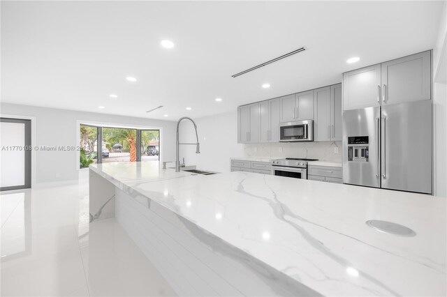 kitchen with a sink, light stone countertops, gray cabinetry, stainless steel appliances, and recessed lighting