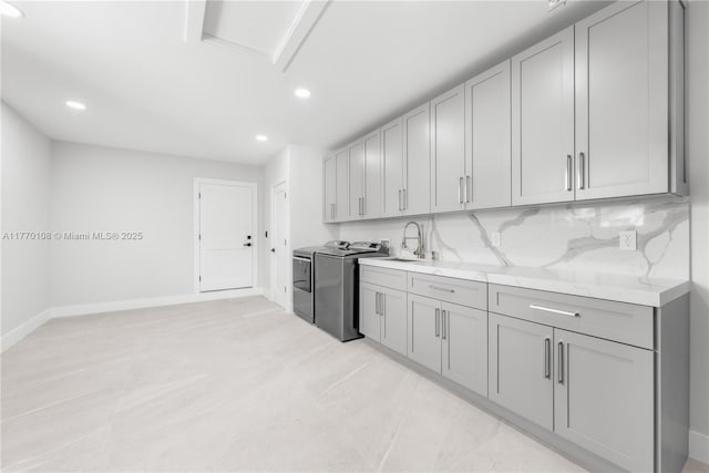 kitchen with gray cabinets, baseboards, decorative backsplash, a sink, and washer and dryer