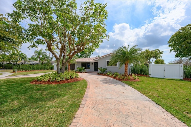 single story home with stucco siding, fence, driveway, a gate, and a front lawn