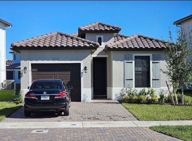 view of front of home featuring a tile roof, stucco siding, decorative driveway, central AC unit, and a garage