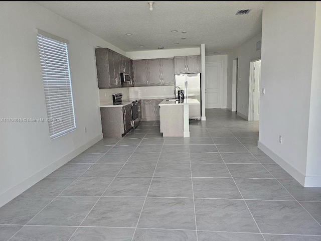kitchen featuring light countertops, stainless steel appliances, a sink, an island with sink, and visible vents