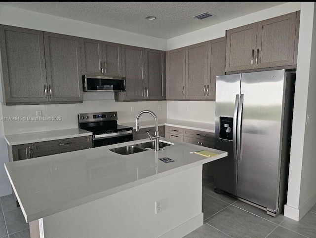 kitchen with a textured ceiling, visible vents, appliances with stainless steel finishes, a sink, and an island with sink