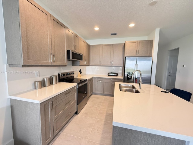 kitchen featuring an island with sink, light countertops, a sink, and stainless steel appliances