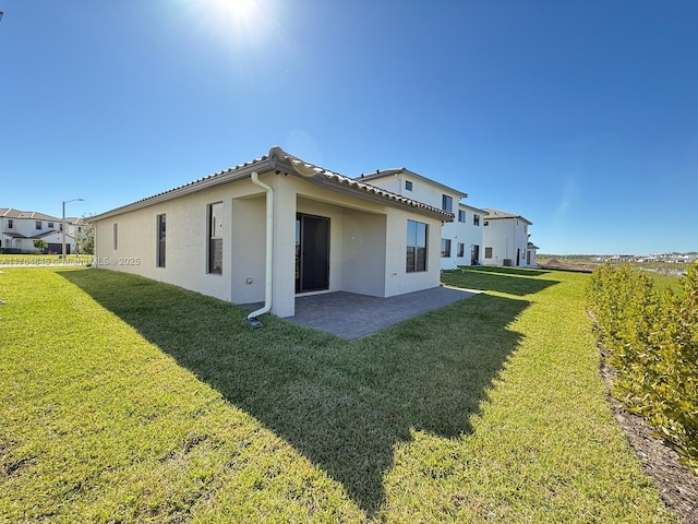 rear view of house with a lawn, stucco siding, and a patio