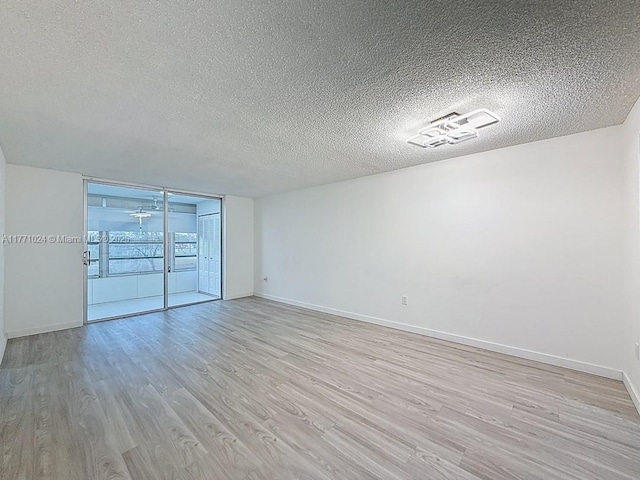 spare room with expansive windows, light wood-style flooring, baseboards, and a textured ceiling