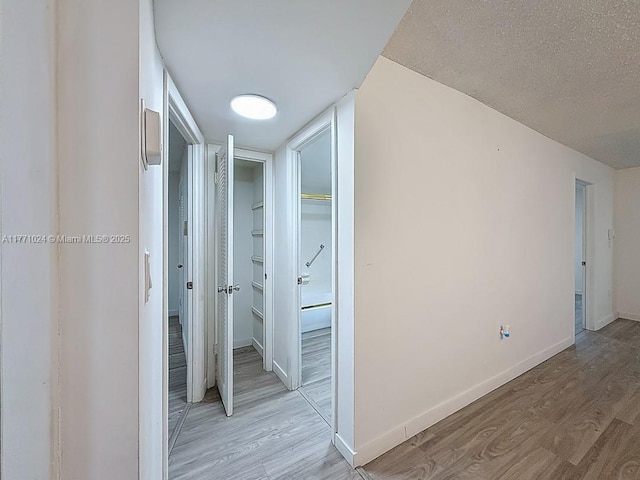 hallway with baseboards, a textured ceiling, and light wood-type flooring