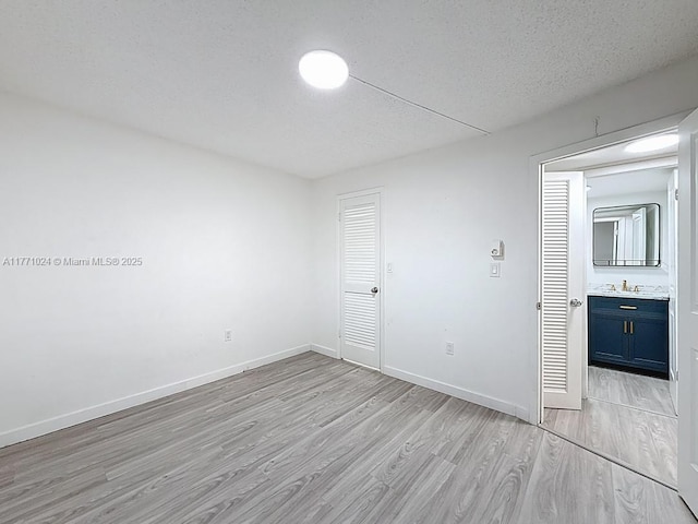 unfurnished room with a sink, a textured ceiling, baseboards, and light wood-type flooring