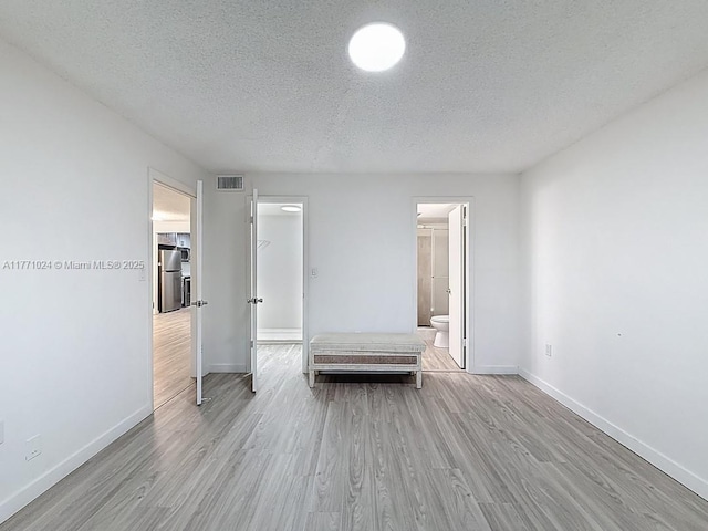 unfurnished bedroom with freestanding refrigerator, wood finished floors, a textured ceiling, baseboards, and visible vents