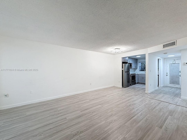 unfurnished living room featuring baseboards, a textured ceiling, visible vents, and light wood-style floors
