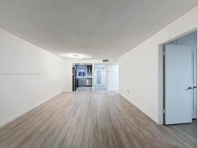 unfurnished living room with baseboards, visible vents, wood finished floors, and a textured ceiling