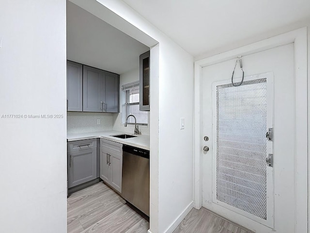 kitchen featuring light countertops, dishwasher, a sink, light wood-style floors, and gray cabinets