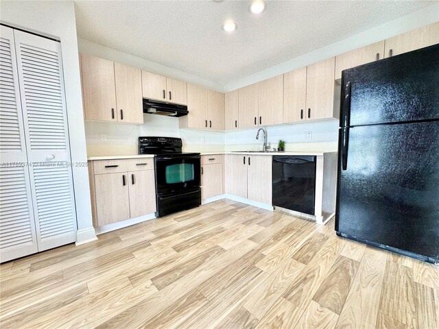 kitchen featuring light brown cabinetry, light wood-style floors, light countertops, under cabinet range hood, and black appliances