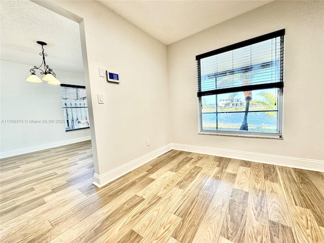empty room with an inviting chandelier, baseboards, and light wood-style flooring