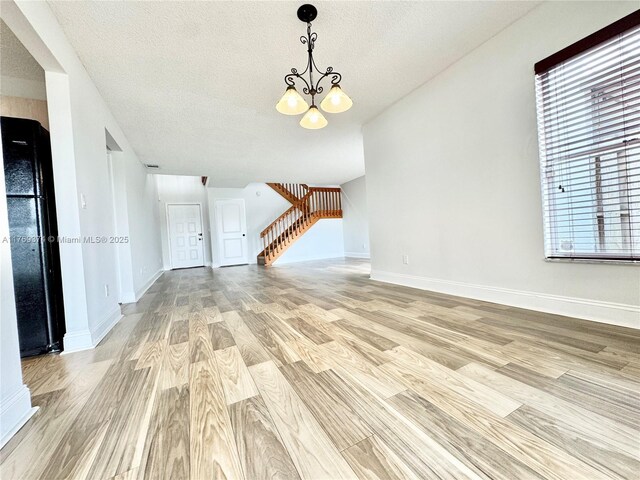 unfurnished living room with stairs, baseboards, a textured ceiling, a chandelier, and light wood-style flooring