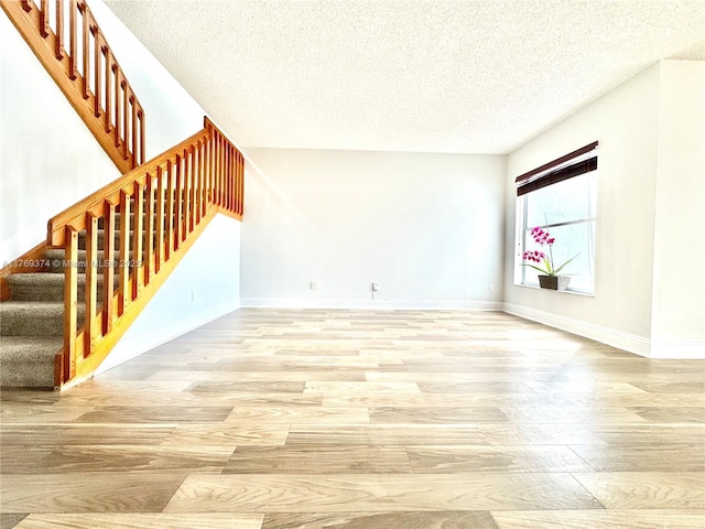 unfurnished living room with stairway, a textured ceiling, baseboards, and wood finished floors
