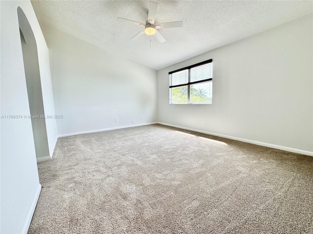 carpeted spare room featuring arched walkways, a textured ceiling, a ceiling fan, baseboards, and vaulted ceiling