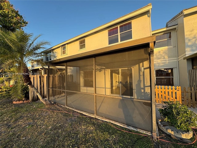 rear view of house featuring fence, stucco siding, and a sunroom