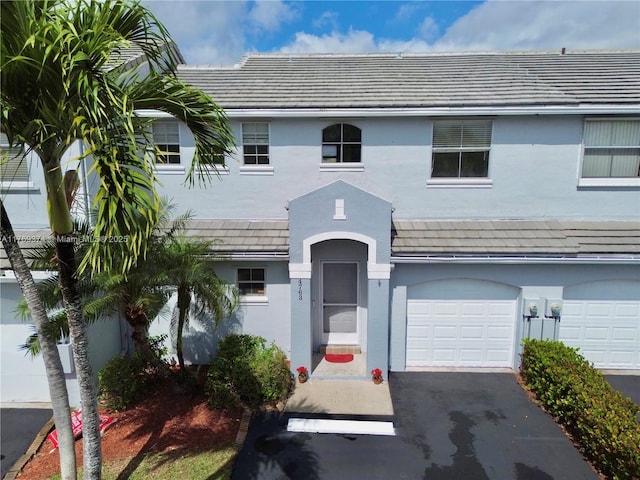view of front of house with a garage, stucco siding, a tile roof, and aphalt driveway