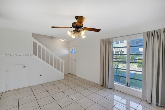 spare room featuring light tile patterned floors, stairway, and a ceiling fan
