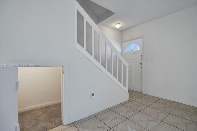carpeted foyer with stairs and baseboards