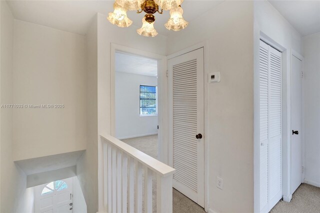 corridor with light carpet, baseboards, an upstairs landing, and a chandelier