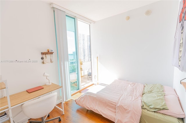 bedroom with a wall of windows, access to exterior, and wood finished floors