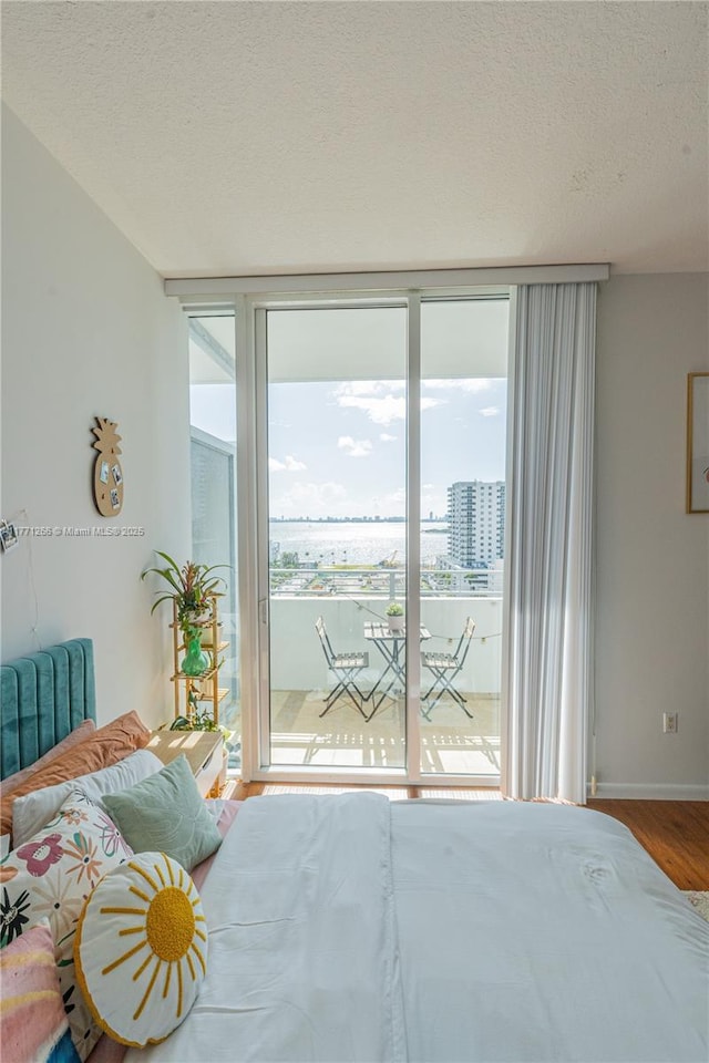 bedroom featuring a wall of windows, access to exterior, wood finished floors, and a textured ceiling