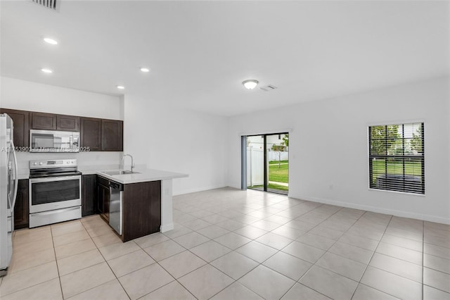 kitchen with open floor plan, a sink, a peninsula, dark brown cabinetry, and appliances with stainless steel finishes