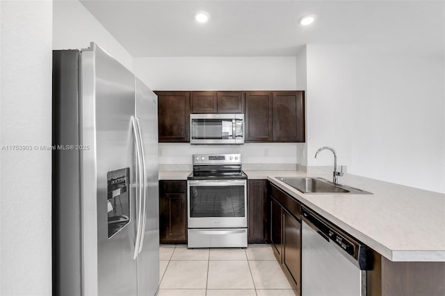 kitchen featuring light tile patterned floors, stainless steel appliances, a sink, a peninsula, and dark brown cabinets