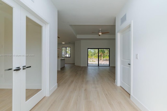 hall featuring baseboards, a tray ceiling, visible vents, and light wood finished floors