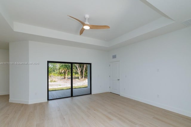 spare room with visible vents, baseboards, a ceiling fan, a raised ceiling, and light wood-style floors