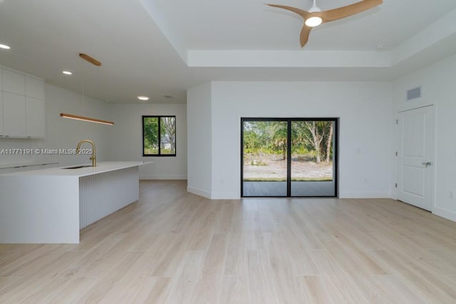 unfurnished living room with visible vents, baseboards, ceiling fan, a sink, and light wood-style floors