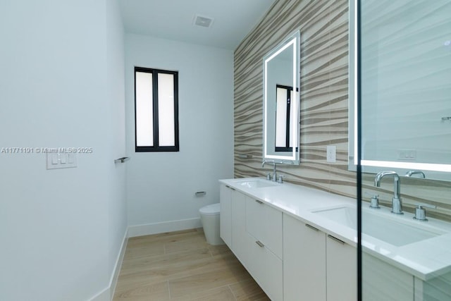 full bath featuring toilet, a sink, double vanity, and baseboards