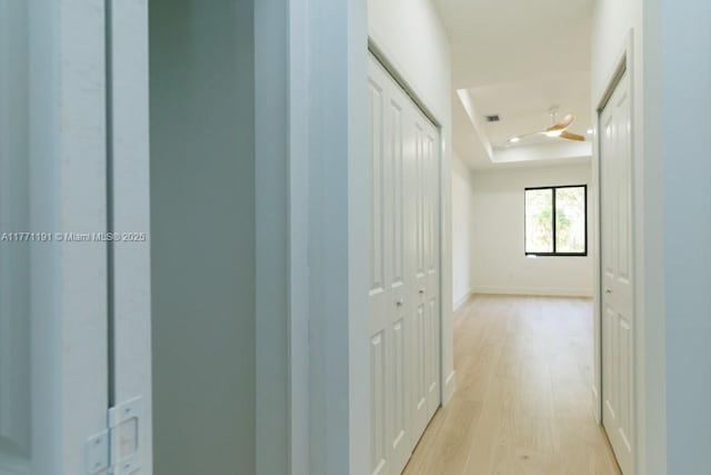 corridor featuring baseboards, a tray ceiling, visible vents, and light wood-style floors