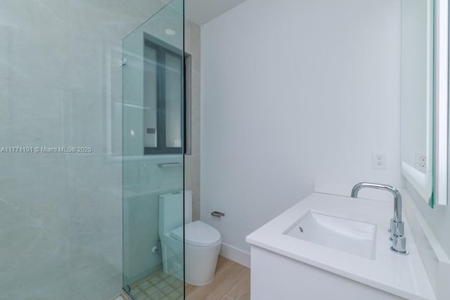 bathroom featuring toilet, vanity, a shower stall, wood finished floors, and baseboards