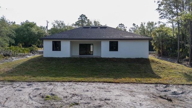 rear view of house with a shingled roof, stucco siding, and a yard
