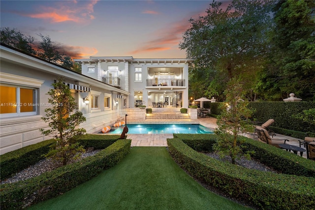 3916 Granada Blvd, Coral Gables, FL 33134 - back of property at dusk with a balcony, a patio, a fenced in pool, stucco siding, and a yard