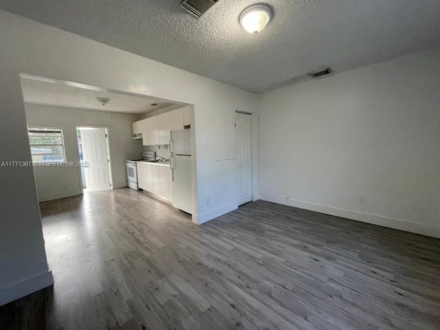 unfurnished living room with baseboards, dark wood-style flooring, a textured ceiling, and visible vents