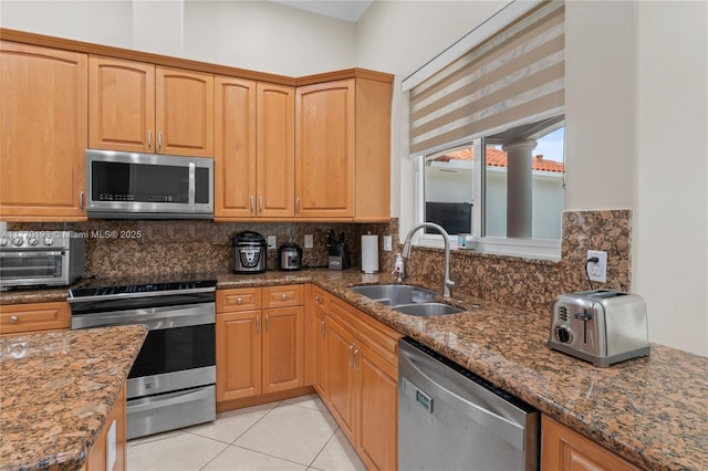 kitchen featuring stainless steel appliances, a sink, dark stone counters, and backsplash