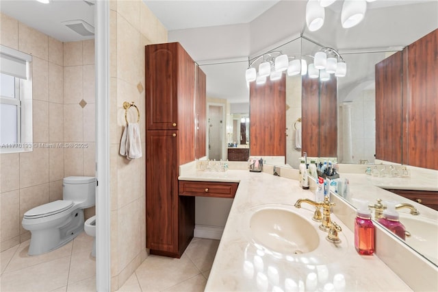 bathroom with tile walls, tile patterned flooring, toilet, a bidet, and vanity