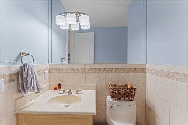 bathroom with toilet, vanity, tile walls, and a chandelier