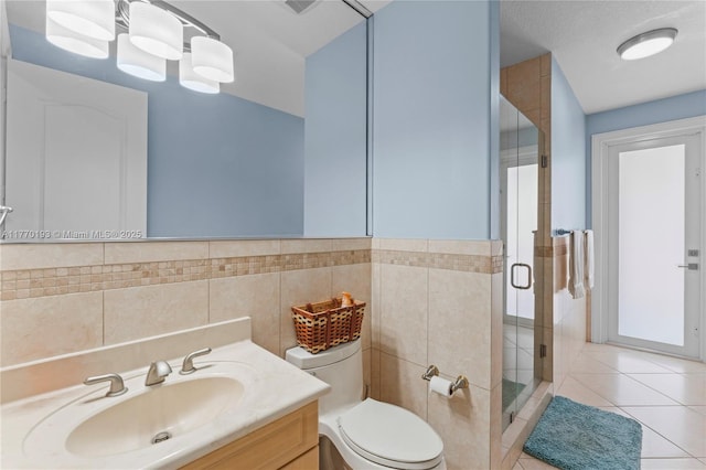 bathroom with tile walls, a stall shower, toilet, vanity, and tile patterned floors