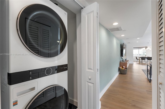 clothes washing area featuring laundry area, visible vents, baseboards, light wood-type flooring, and stacked washer / drying machine
