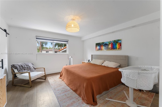 bedroom with baseboards, a barn door, and wood finished floors