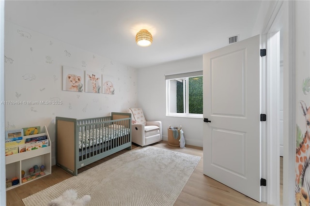 bedroom with a crib, wood finished floors, and visible vents