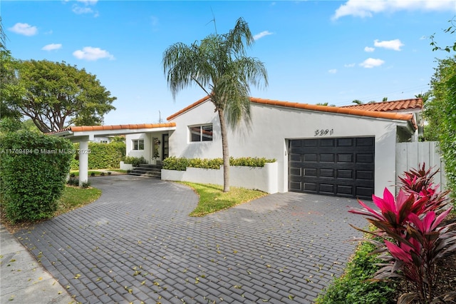 view of front of property featuring a tile roof, decorative driveway, fence, an attached garage, and stucco siding