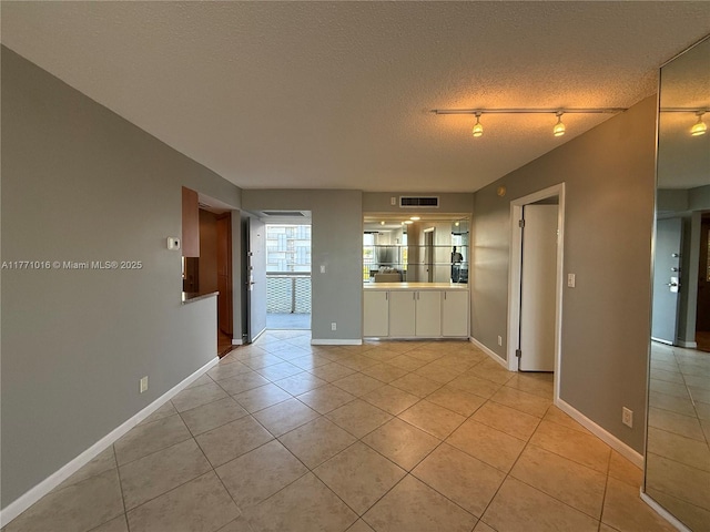 unfurnished living room featuring baseboards, visible vents, a textured ceiling, and light tile patterned flooring