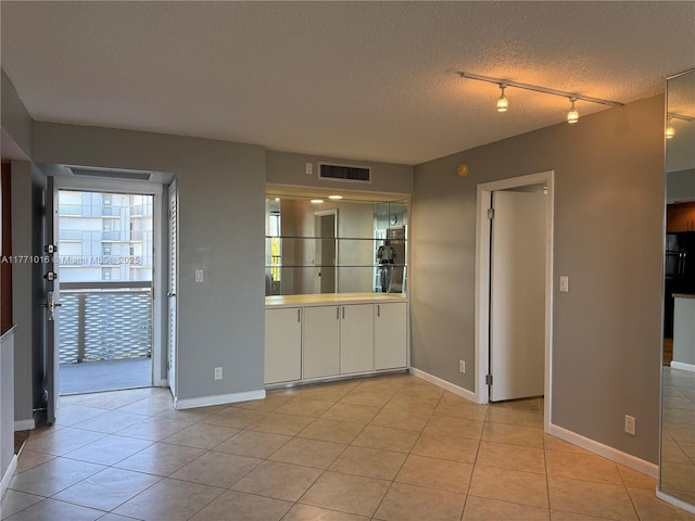 spare room featuring light tile patterned floors, track lighting, visible vents, baseboards, and a textured ceiling
