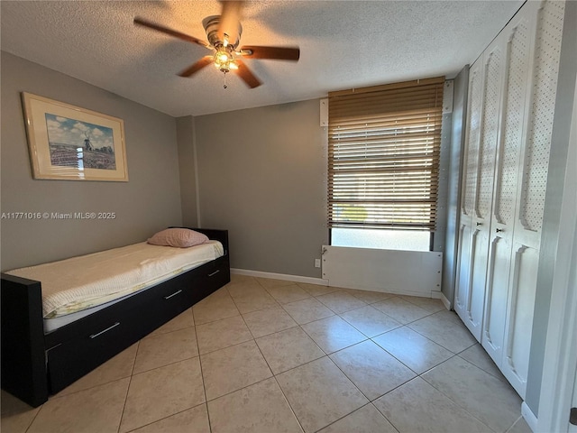 bedroom with a textured ceiling, ceiling fan, light tile patterned flooring, and baseboards